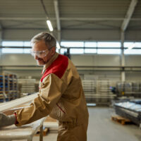 Happy manual worker making wood furniture at carpentry workshop.